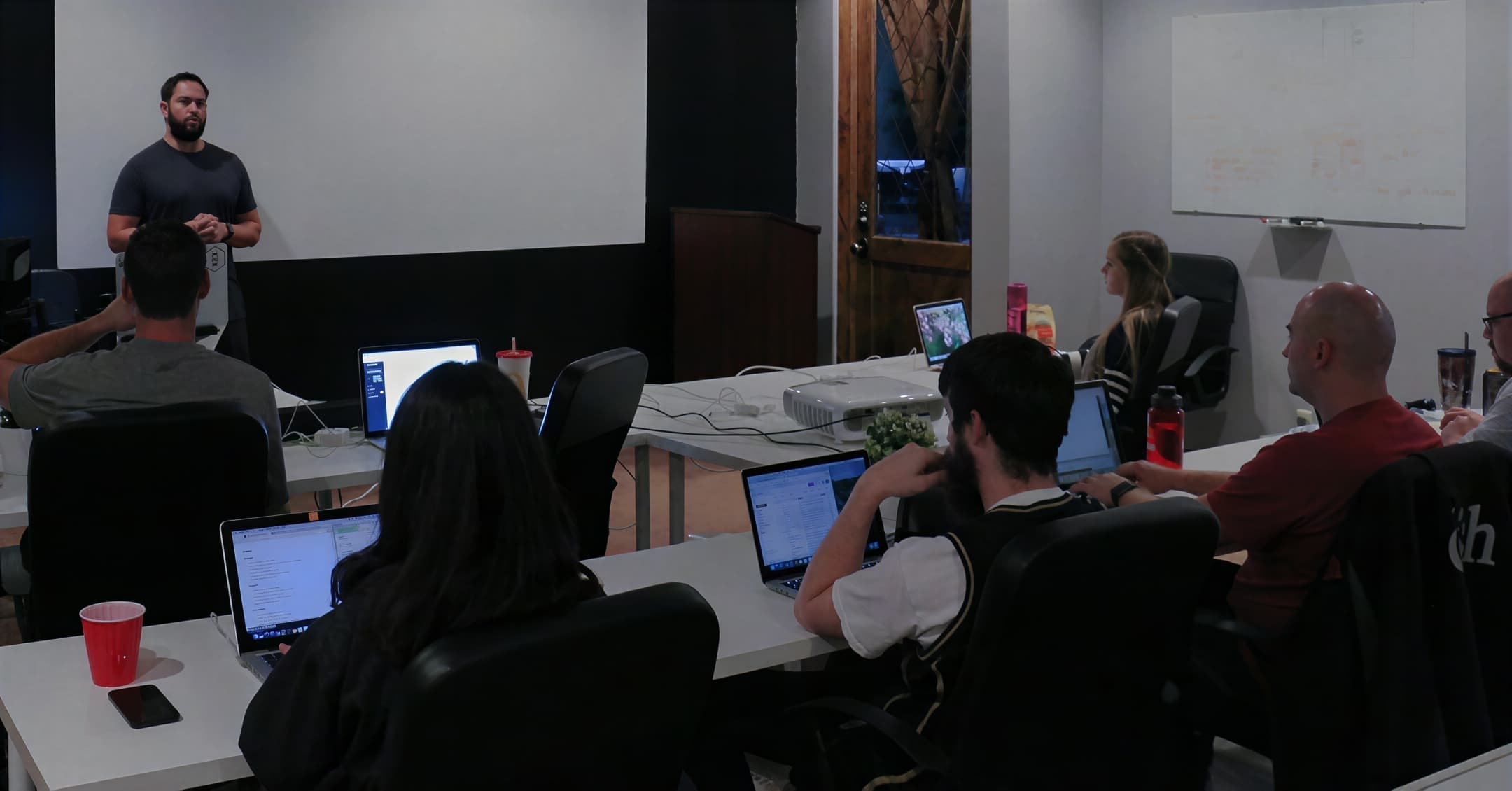 Jordan leading an instructor workshop with participants gathered around tables and laptops