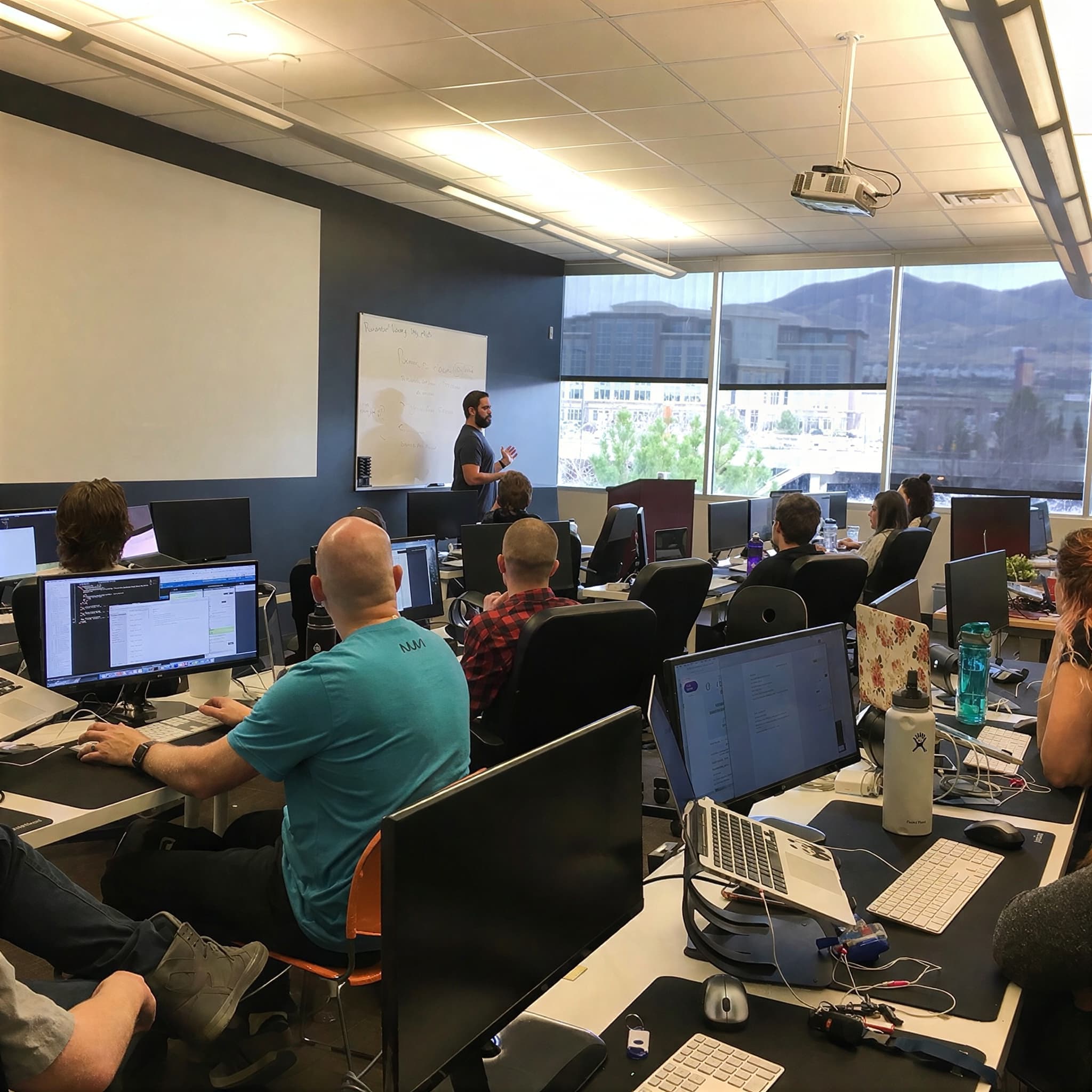 Developers at their workstations listening to Jordan teach beside a whiteboard